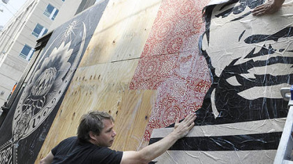 Shepard Fairey puts up a poster on a wall across the street from the Warhol Museum on the North Shore.