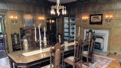 The dining room features oak paneling, an original chandelier and silver wall sconces. It overlooks the back lawn.