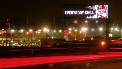 A Cola-Cola advertisement on a digital billboard dominates the night sky along a roadway in Cleveland.