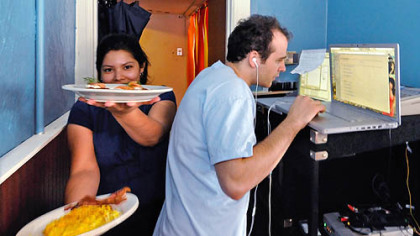 Waffle Shop waitress Zena Ruiz squeezes past "Psychic Radio" producer Terrence Boyd in the hallway from the kitchen, which also serves as the control room. Mr. Boyd juggles two laptops and video control station as he randomly switches radio feeds to anchor Dawn Waleski and maintains the Internet broadcast.
