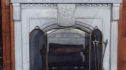 The coat of arms in the center of this carved stone fireplace depicts a knight with a branch hovering above him.