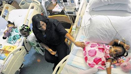 Catherine Nickson fixes her daughter Dagian Lee's dress while her other daughters Danielle Lee (in bed) and Dayloni Lee play with a toy guitar in their room at Children's Hospital yesterday.  Conjoined twins Dagian and Danielle were recently separated at Children's Hospital.