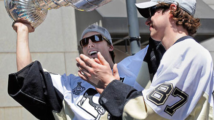 Penguins goalie Marc-Andry Fleury holds up the Stanley Cup as he rides with captain Sidney Crosby along Grant Street.