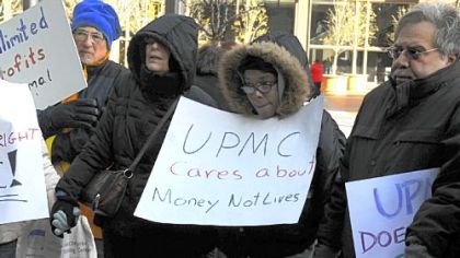 Linda Lenno, of Braddock, uses her chin to hold a sign Friday during a prayer vigil to save Braddock hospital near the U.S. Steel Tower on Grant Street. UPMC has offices there.