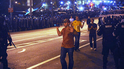 Several people caught between riot police walk with their hands raised toward the police line as it funneled protesters into the lawn of the Cathedral of Learning in Oakland.