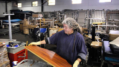 Surrounded by donated medical equipment, Robin Checkley re-stains a table in Global Links' warehouse.