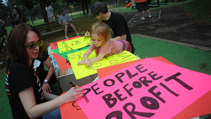 Keira Lee Gibson, 3, of Lawrenceville, watches as Maureen Sandefer of Boulder, Colorado creates a sign as people start to gather in Arsenal Park in Lawrenceville for an unpermitted march to Downtown.